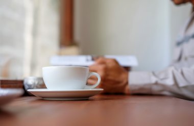 Beyaz kahve Kupası açık bir kitap okurken erkek koyun.