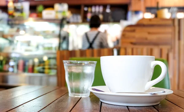 Weiße Kaffeetasse und Glaswasser auf Holztisch mit verschwommenem — Stockfoto