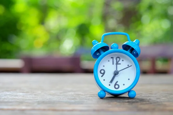 Sete horas, despertador azul em madeira com verde desfocado de volta — Fotografia de Stock