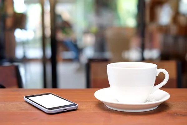Vit kaffekopp och smart phone på träbord med suddiga ca — Stockfoto