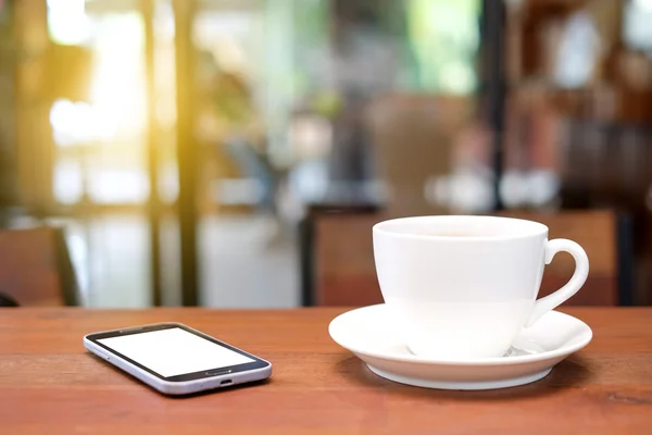 Vit kaffekopp och smart phone på träbord med suddiga ca — Stockfoto