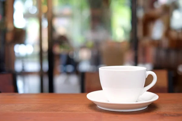 Чашка белого кофе на деревянном столе с размытым фоном кафе . — стоковое фото