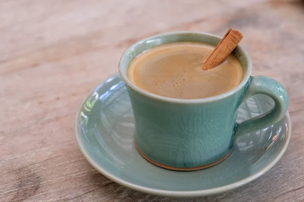 Coffee cup on wooden table with cinnamon in coffee. — Stock Photo, Image