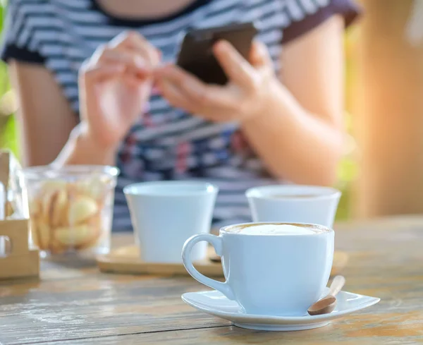 Vit kaffekopp på träbord med människor spelar smart p — Stockfoto