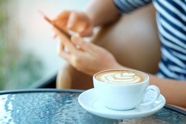 Kahve kalp latte ile akıllı telefon elinde oynayan kadınlar giy