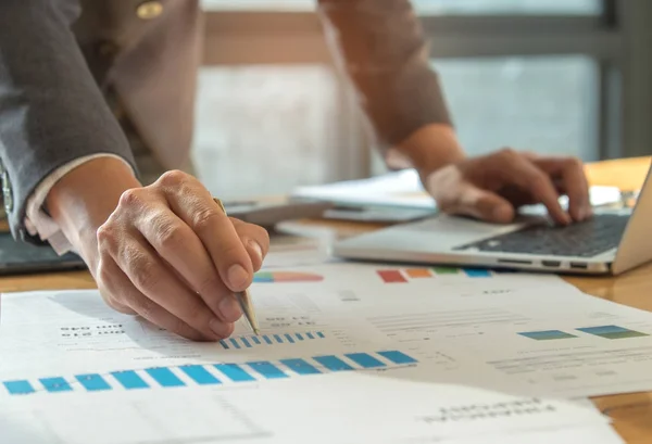 Geschäftsmann zeigt mit Stift auf Grafik und benutzt Laptop. — Stockfoto