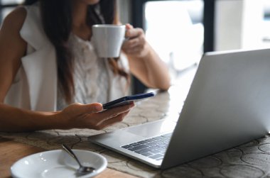Kadın işadamları kahve içiyorlar ve akıllı telefon kullanıyorlar. Kahve freni ve masadaki dizüstü bilgisayar arasında çalışıyor..
