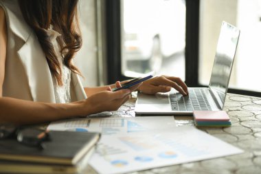 İş kadınları şirket performans defterini kontrol ediyor. Elinde bir akıllı telefon ve ofiste bir dizüstü bilgisayar tutuyor..