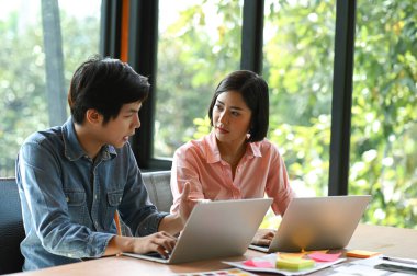 Yeni nesil genç kadın ve erkekler ofis masasında oturuyor, danışmanlık yapıyor, çalışıyor ve dizüstü bilgisayar kullanıyorlar..
