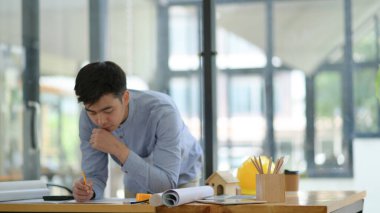 Mühendislik ofisteki kat planlarını kontrol ediyor. Elinde bir kalem tuttu ve zemin planına ciddi ciddi baktı..