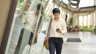 Yeni nesil omuz çantalı bir iş adamı işi kontrol etmek için akıllı telefona bakar..