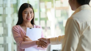 Genç kadın ve erkeklerin modern ofiste mutlu bir şekilde el sıkışması ve gülümsemesi..