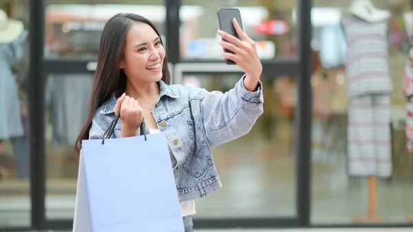 アジアの買い物客はスマートフォンを使って自撮りをしています 彼女は立って買い物袋を持っていた — ストック写真