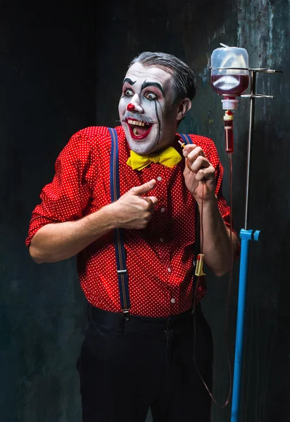 De enge clown en infuus met bloed op dack achtergrond. Halloween concept — Stockfoto