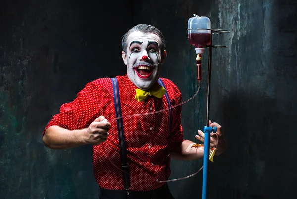 De enge clown en infuus met bloed op dack achtergrond. Halloween concept — Stockfoto