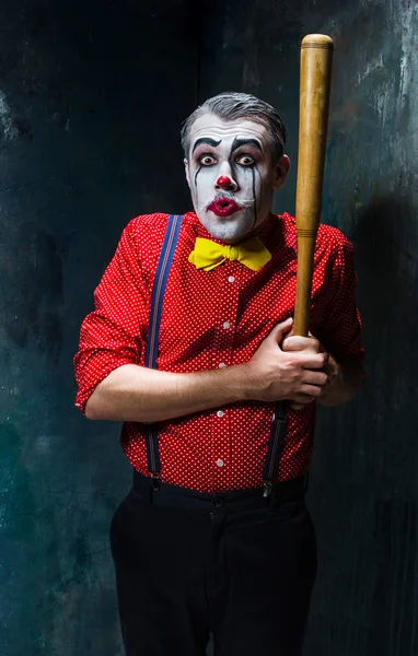 The scary clown and baseball-bat on dack background. Halloween concept