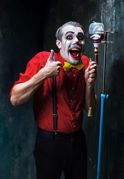 De enge clown en infuus met bloed op dack achtergrond. Halloween concept — Stockfoto