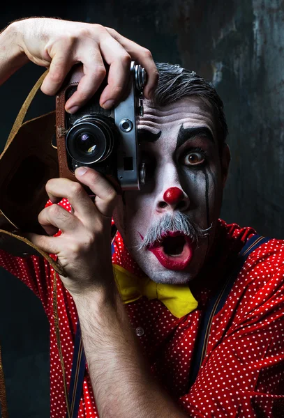 De enge clown en een camera op dack achtergrond. Halloween concept — Stockfoto