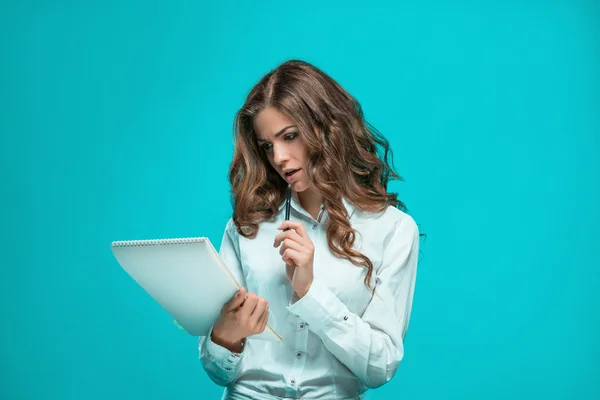 Удумлива молода бізнес-леді з ручкою і планшетом для нотаток на синьому фоні — стокове фото