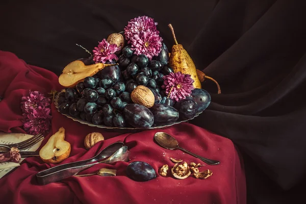 Плодовая чаша с виноградом и сливами против бордового скатерти — стоковое фото