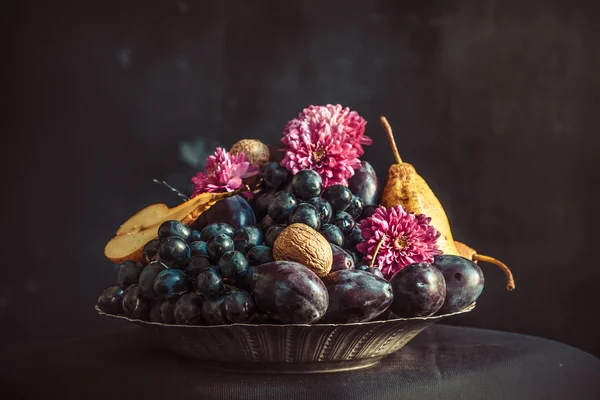 El frutero con uvas y ciruelas contra una pared oscura — Foto de Stock