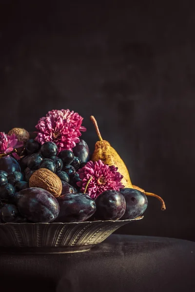El frutero con uvas y ciruelas contra una pared oscura — Foto de Stock