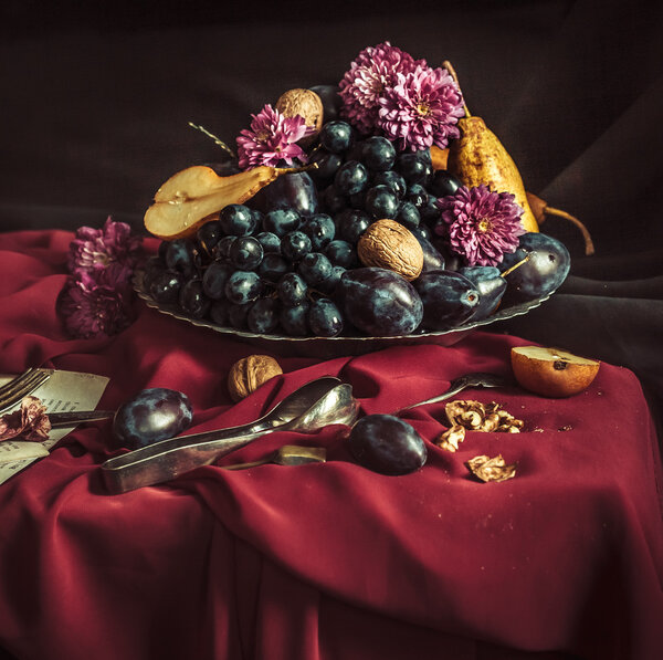 The fruit bowl with grapes and plums against a maroon tablecloth