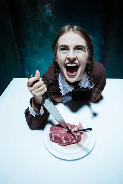 Sangrento tema de Halloween: menina louca com uma faca, garfo e carne — Fotografia de Stock