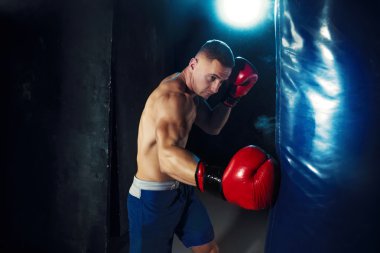 Erkek boxer kum torbası içinde karanlık bir stüdyoda dramatik sinirli aydınlatma ile boks