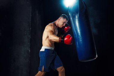 Erkek boxer kum torbası içinde karanlık bir stüdyoda dramatik sinirli aydınlatma ile boks
