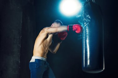 Erkek boxer kum torbası içinde karanlık bir stüdyoda dramatik sinirli aydınlatma ile boks