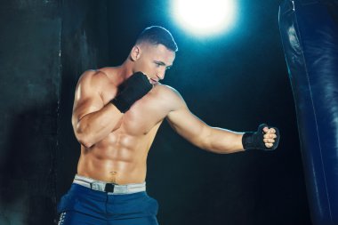 Erkek boxer kum torbası içinde karanlık bir stüdyoda dramatik sinirli aydınlatma ile boks