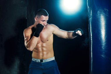 Erkek boxer kum torbası içinde karanlık bir stüdyoda dramatik sinirli aydınlatma ile boks