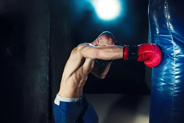 男性的拳击手拳击沙袋在与戏剧性的前卫照明，在一个黑暗的工作室 — 图库照片