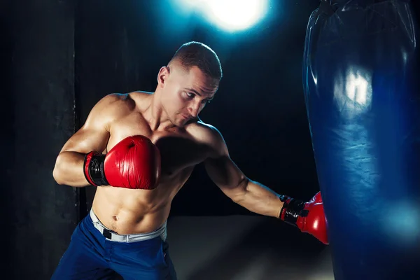 Mies nyrkkeilijä nyrkkeily nyrkkeilysäkissä dramaattinen särmikäs valaistus pimeässä studiossa — kuvapankkivalokuva