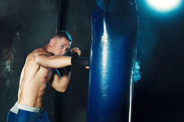 Boxe masculine boxe dans un sac de boxe avec éclairage intense dramatique dans un studio sombre — Photo