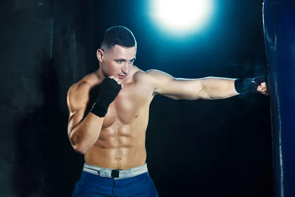 男性的拳击手拳击沙袋在与戏剧性的前卫照明，在一个黑暗的工作室 — 图库照片