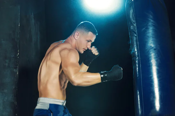 Boxe boxeador masculino em saco de perfuração com iluminação nervosa dramática em um estúdio escuro — Fotografia de Stock