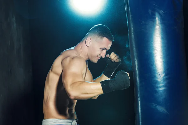 Boxe boxeador masculino em saco de perfuração com iluminação nervosa dramática em um estúdio escuro — Fotografia de Stock