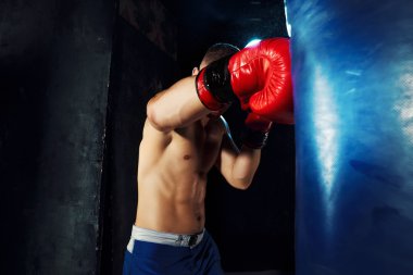 Erkek boxer kum torbası içinde karanlık bir stüdyoda dramatik sinirli aydınlatma ile boks