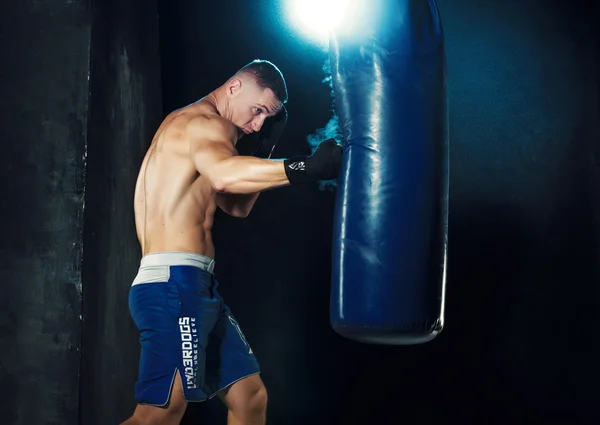 Boxe boxeador masculino em saco de perfuração com iluminação nervosa dramática em um estúdio escuro — Fotografia de Stock