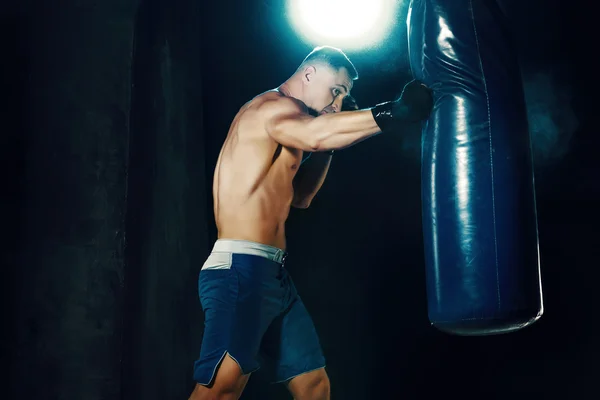 男性ボクサー ボクシング バッグをパンチで暗いスタジオで劇的なエッジの効いた照明 — ストック写真