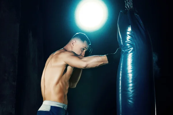 Boxeo boxeador masculino en saco de boxeo con iluminación dramática y vanguardista en un estudio oscuro —  Fotos de Stock