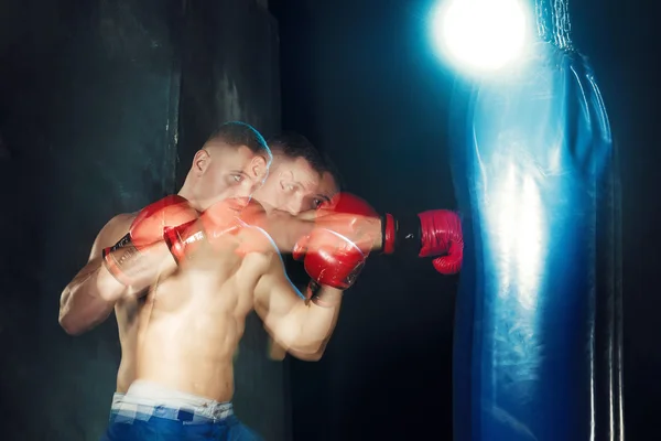 Male boxer boxing in punching bag with dramatic edgy lighting in a dark studio — Stock Photo, Image