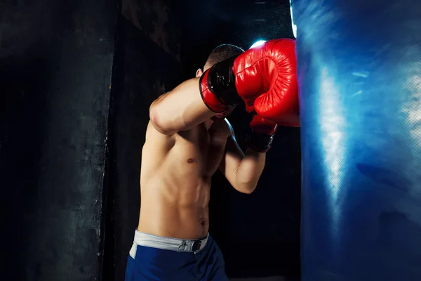 Boxe boxeador masculino em saco de perfuração com iluminação nervosa dramática em um estúdio escuro — Fotografia de Stock