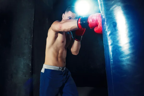Мужской боксерский бокс в боксерской груше с драматическим резким освещением в темной студии — стоковое фото
