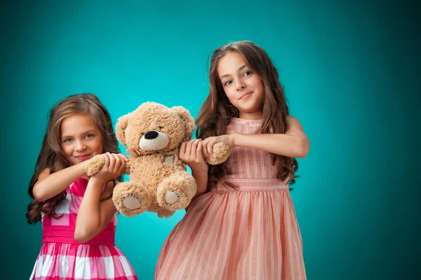 Die beiden niedlichen kleinen Mädchen auf blauem Hintergrund mit Teddybär — Stockfoto