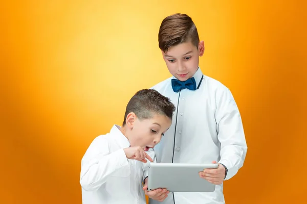 De twee jongens met behulp van de laptop op een oranje achtergrond — Stockfoto