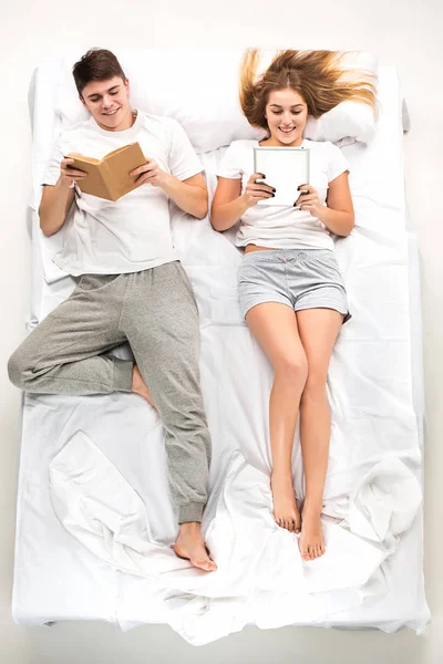 La joven pareja adorable acostada en una cama con libros —  Fotos de Stock