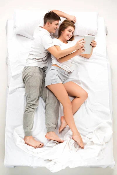 La joven pareja encantadora acostada en una cama con portátil —  Fotos de Stock